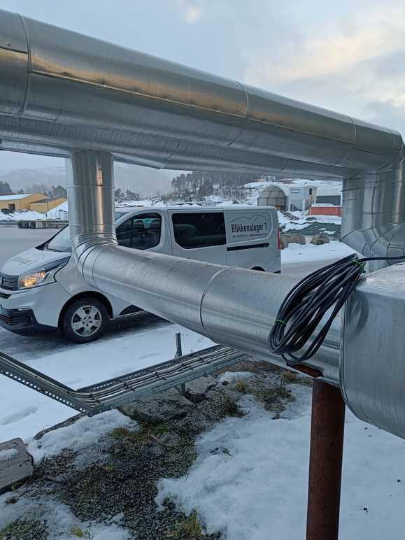 Rørledninger i metall med en varebil i bakgrunnen, dekket av snø og is.