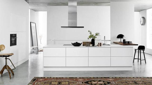 Moderne kjøkken med hvite skap, en stor øy, og en stilren stol på et teppe. Minimalistisk design og lys atmosfære.
