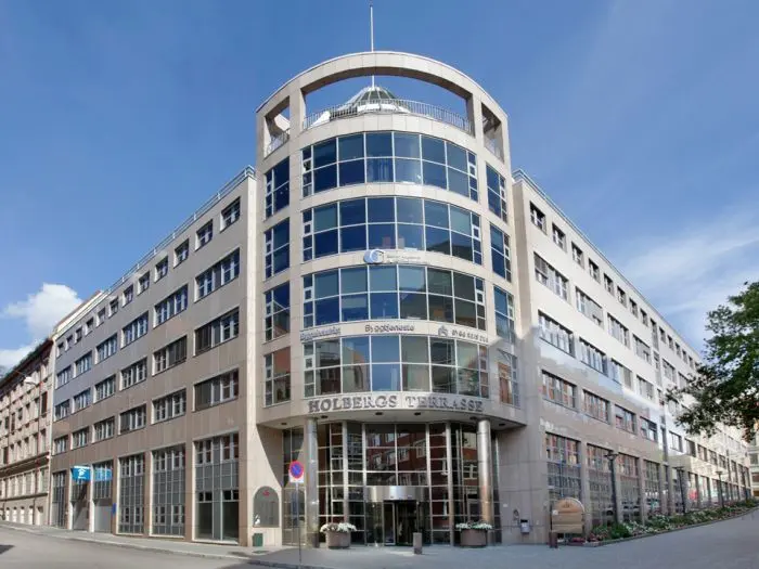 Moderne kontorbygg med store vinduer og en karakteristisk inngang, beliggende i en bygate.