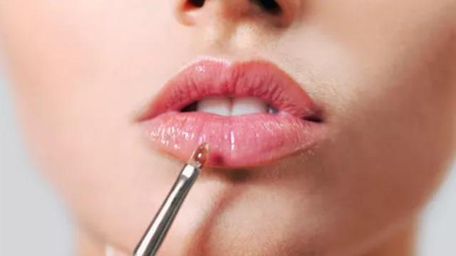 Nærbilde av en kvinne som påfører lipgloss på leppene med en applikator.