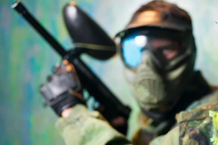 En soldat i kamuflasje holder en paintball-markør, iført maske og beskyttelsesbriller.