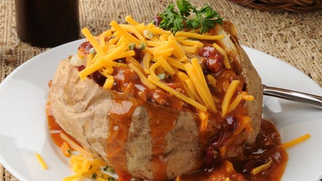 En bakt potet med chili, ost og urter på en hvit tallerken, ser appetittvekkende ut.