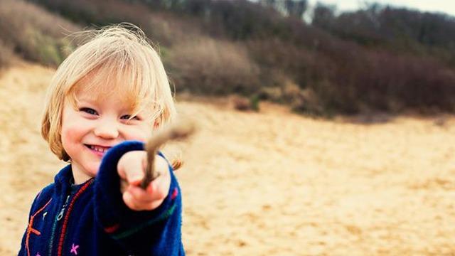 Liten gutt smiler og peker med en pinne på en sanddyne i naturen.