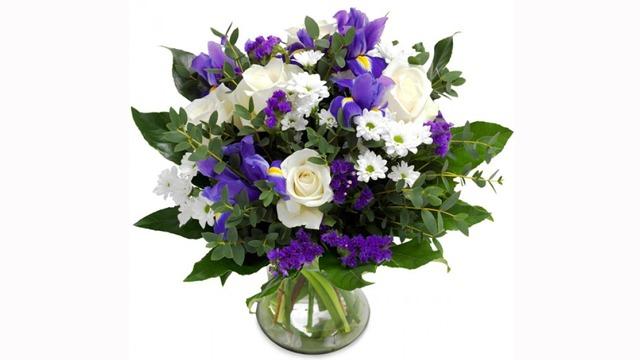 En vakker bukett med hvite roser, lilla iris, og forskjellige blomster i en glassvase.
