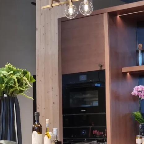 Moderne kjøkkeninnredning med trepanel, innebygd ovn, planter og stilige lamper.