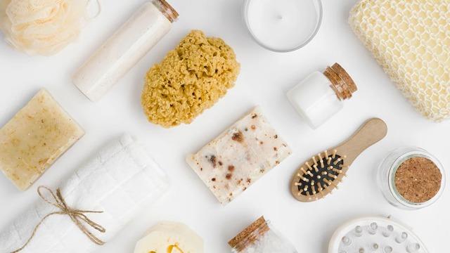 Bilde av ulike badeprodukter som såpe, svamp, lys, og krukker med naturlige ingredienser på en hvit bakgrunn.