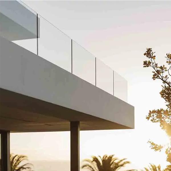 Moderne hus med glassrekkverk og solnedgang i bakgrunnen, palmer synlige i horisonten.