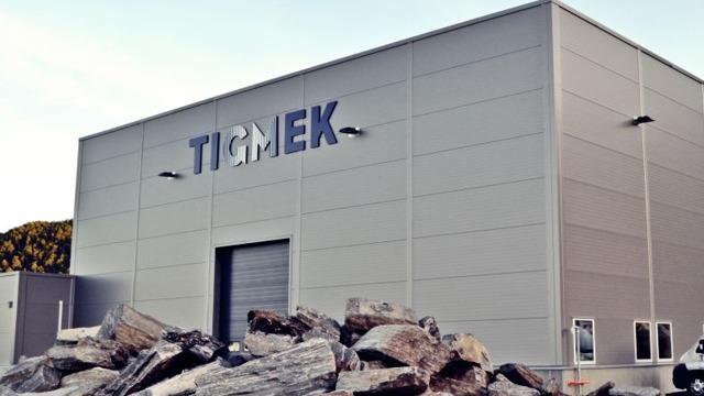 Moderne industribygg med navnet "TIGMEK" på fasaden, omgitt av store steiner.