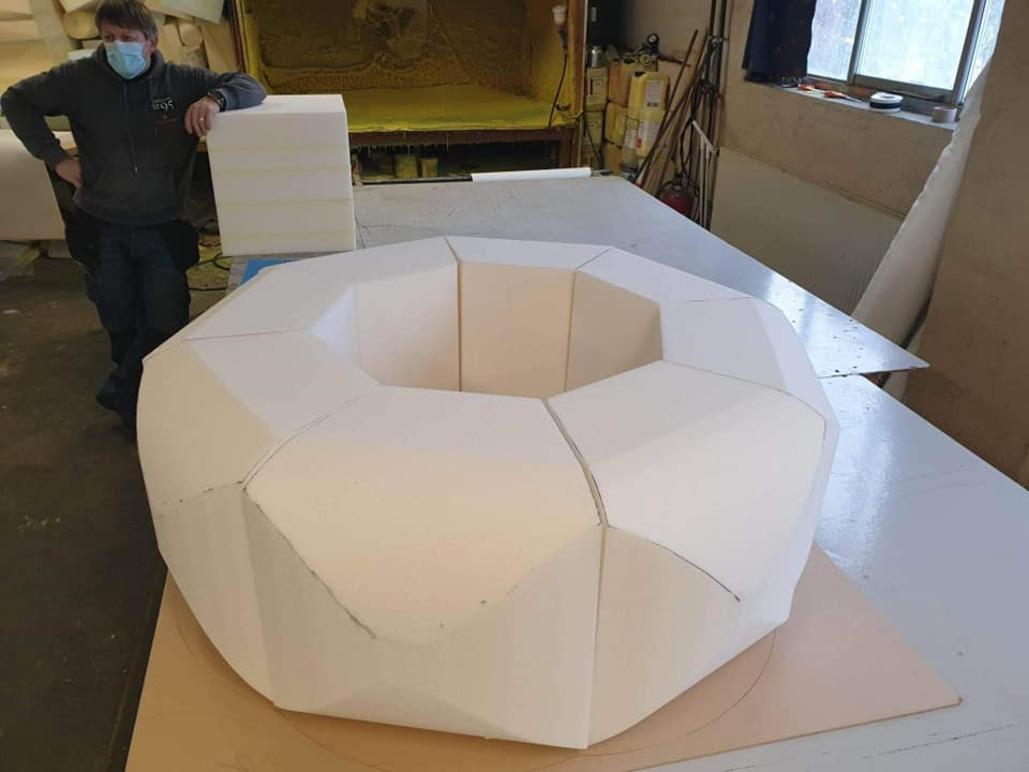 En person i munnbind står ved siden av en stor, hvit, geometrisk form laget av skum.