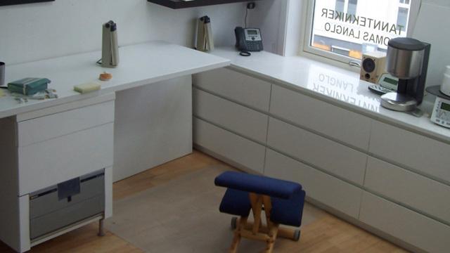 Moderne kontor med hvite skap, skrivebord og en ergonomisk stol i et lyst rom.