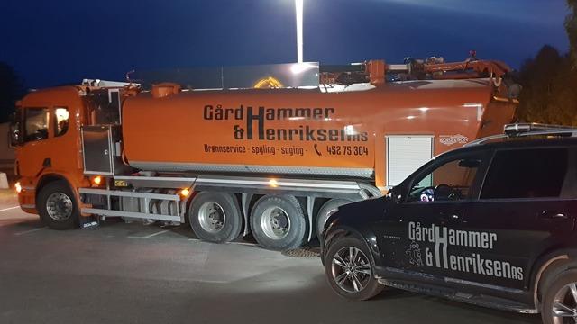 Lastebil med påbygg fra Gård Hammer & Henriksen parkert om kvelden, med en SUV ved siden av.