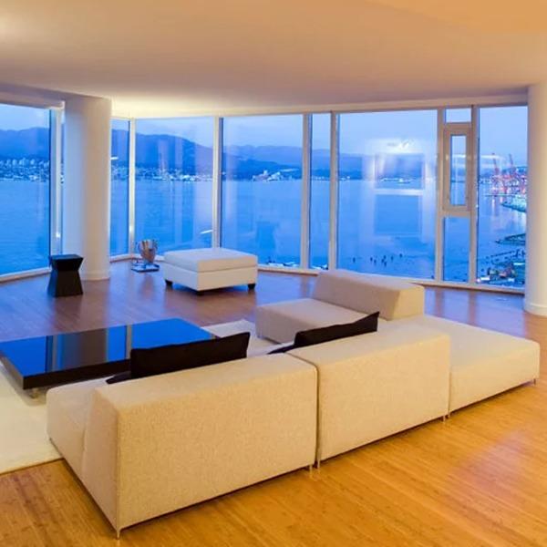 Moderne stue med stor sofa, lavt bord og panoramavinduer som viser havutsikt ved skumring.