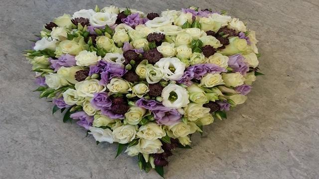 Et hjerteformet blomsterarrangement med hvite, lilla og grønne blomster.