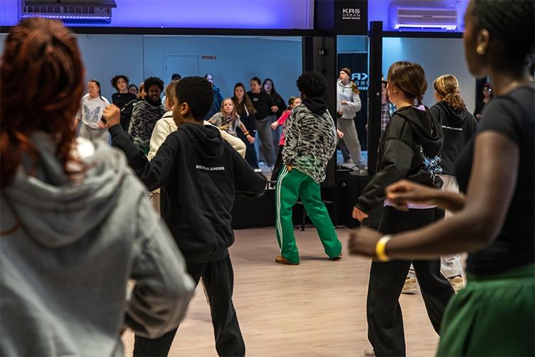 Ungdommer danser i en moderne dansestudio med speil og fargerik belysning.