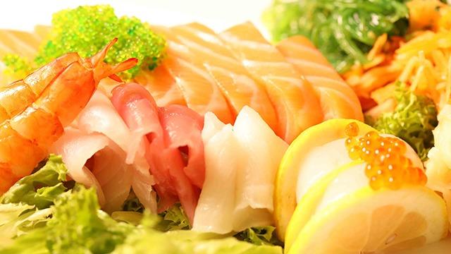 Fersk sushi med laks, reker, tunfisk og sitron på en seng av salat.