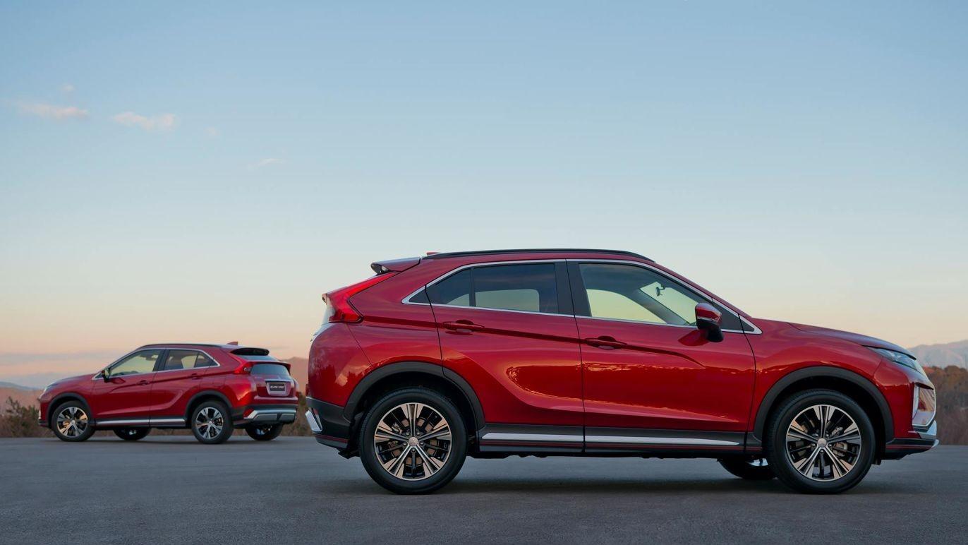 To biler parkert på en vei, med en rød SUV i forgrunnen og en grå SUV i bakgrunnen under en klar himmel.