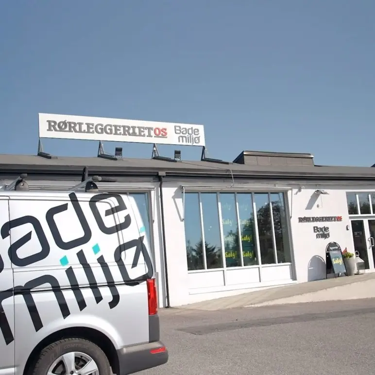 Bilde av Rørleggeriet OS med logoen Bade Miljø på en varebil foran bygningen. Klart blå himmel i bakgrunnen.