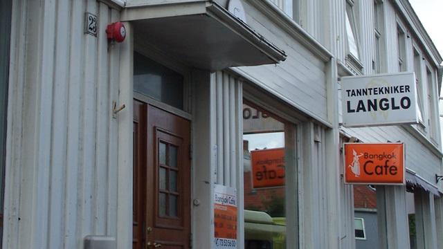 Inngangspartiet til tannklinikken Langlo med en cafe ved siden av. Bygningen har hvite vegger og store vinduer.