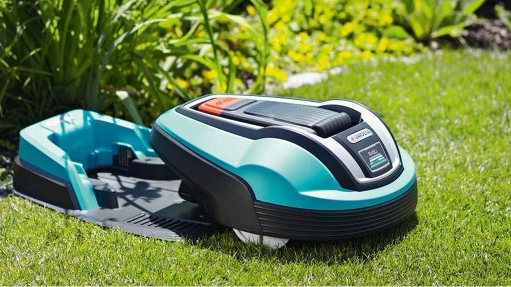 En robotgressklipper står på gresset i hagen, omgitt av grønne planter og busker.