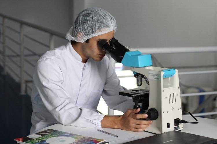 En forsker i hvit frakk ser gjennom et mikroskop i et laboratorium.