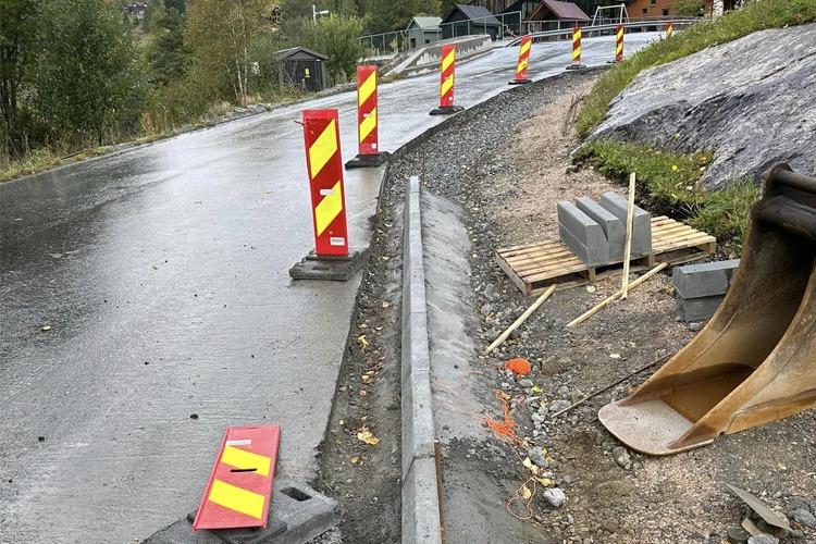 Veiarbeid med avsperringer og grus på en regnvåt vei i et fjellområde.