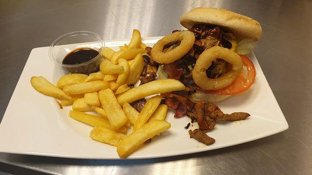 En tallerken med en hamburger med løkringer, salat og tomat, servert med pommes frites og en saus.