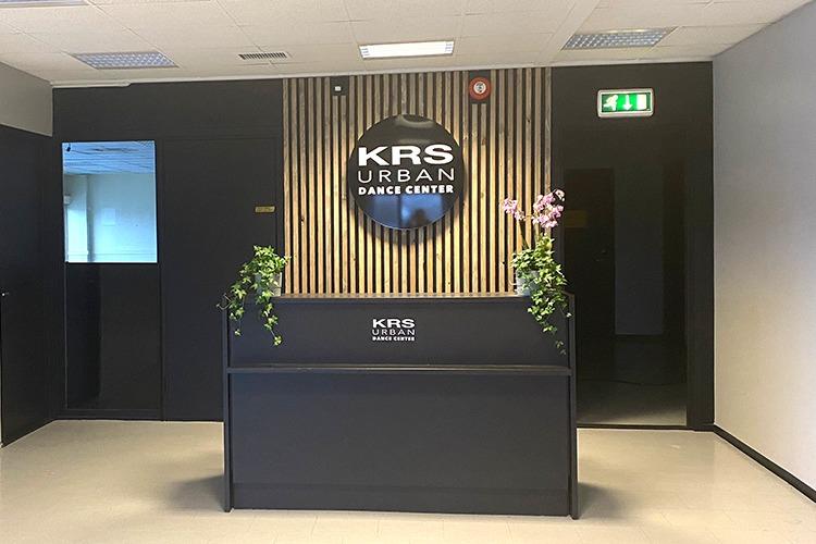 Moderne resepsjon ved KRS Urban Senter med planter og logo på veggen.
