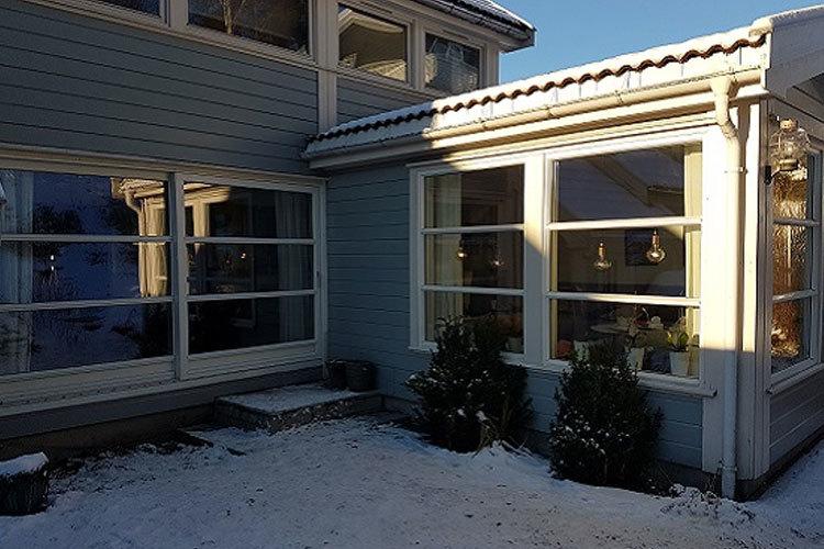 Moderne hus med store vinduer, snø på bakken og sollys som skinner på fasaden.
