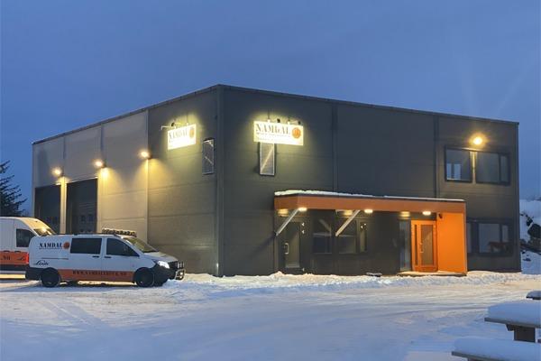 Moderne bygning med snødekt inngang og opplyste skilt, beliggende i et vinterlandskap.