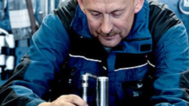 En mann i arbeidsklær undersøker verktøy på en arbeidsbenk i et verksted.