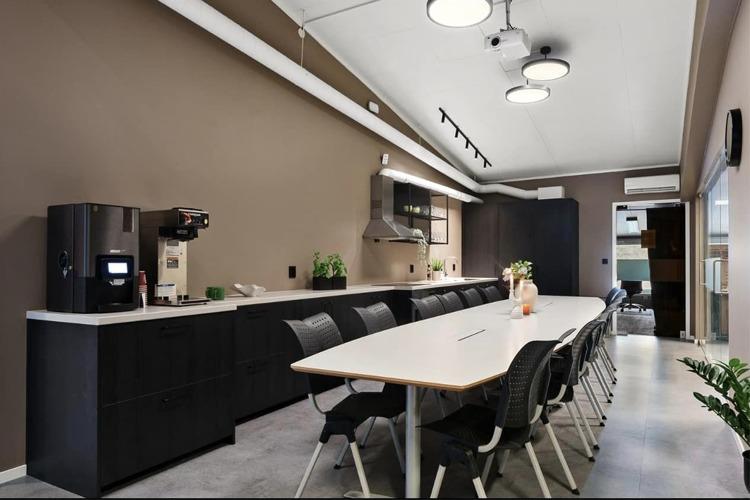 Moderne kjøkken med lang spisebord, svarte stoler og kaffemaskin på benken. Veggene er malt i brune toner.