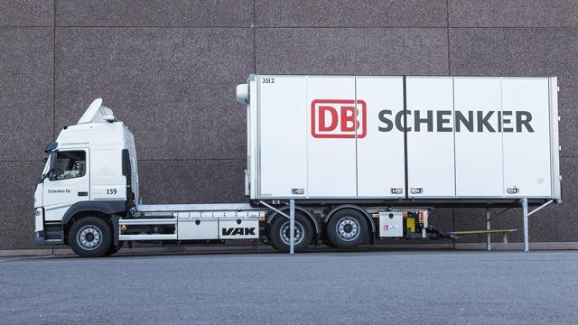 En lastebil fra DB Schenker med en stor container parkert ved en murvegg.