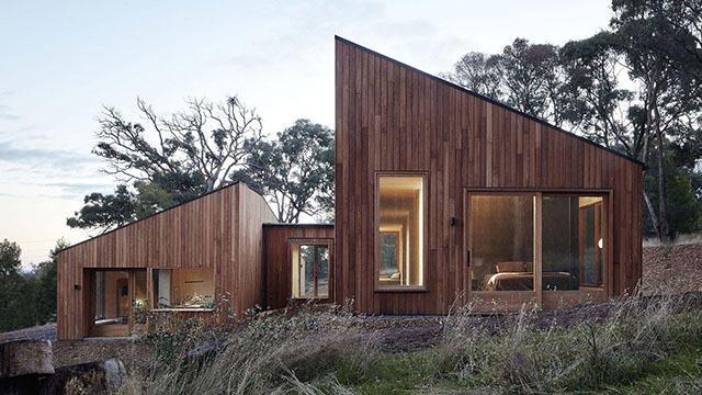 Moderne hus med trekledning og store vinduer, omringet av natur og gress.