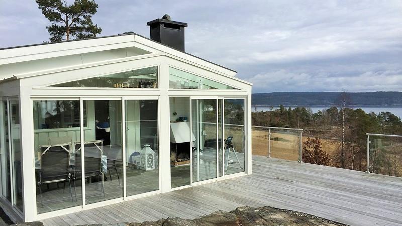 Moderne glassveranda med utsikt over vannet og omgivelsene, plassert på en tredekk.