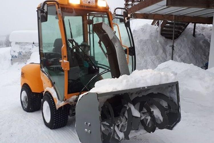 En snøfreser i snøen, parkert ved en hytte med snødekte omgivelser.