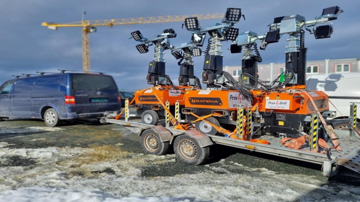 Lysmaster på tilhenger med en varebil i bakgrunnen, plassert på en byggeplass med snø.