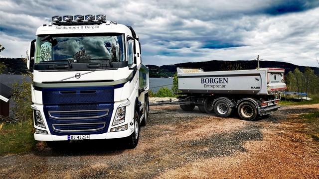 En stor lastebil fra Volvo med tilhenger, parkert ved en innsjø under en dramatisk skyhimmel.