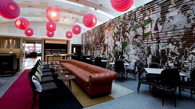 Moderne kaféinnredning med en stor brun sofa, stilige stoler og fargerike lamper i taket.