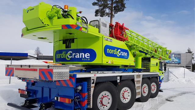 En stor, grønn kranbil fra Nordic Crane står på snøen med en rød kranarm og tydelig logo.