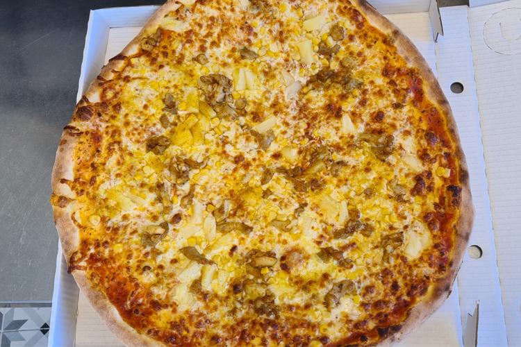 En stor pizza med ananas, kjøttdeig og ost, servert i en pappeske.