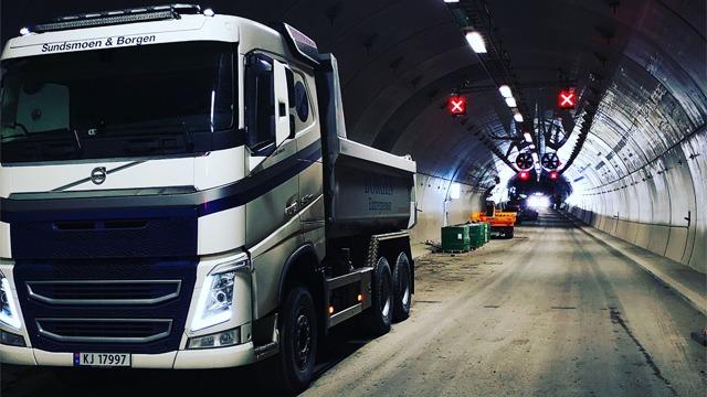 En stor lastebil står i en tunnel med røde lys og en tunnelboremaskin i bakgrunnen.