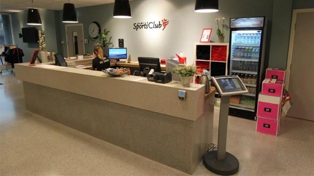 Moderne resepsjon med en ansatt, datamaskin, planter og en automat med drikkevarer.