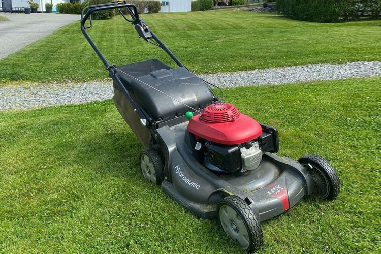 Gressklipper med rød motor stående på grønt gress i hagen, klar til bruk.