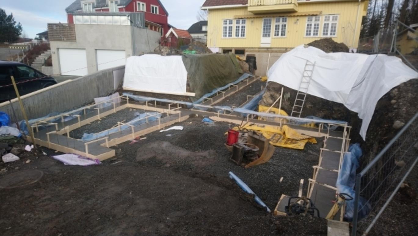 Byggeplass med stillas, materialer og arbeidere som jobber med konstruksjon av en ny bygning.