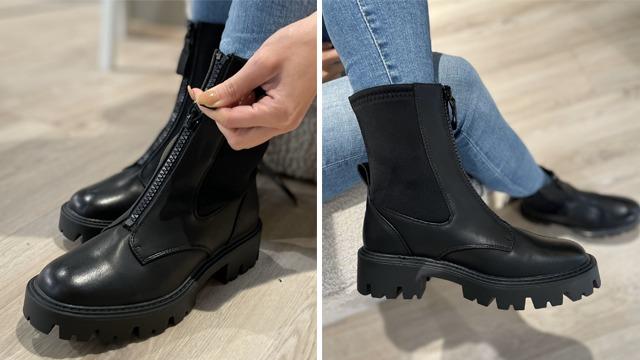 Svart ankelstøvlett med glidelås, iført av en person med jeans, på et lyst tregulv.
