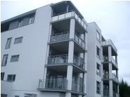 Moderne leilighetsbygg med flere balkonger og glassrekkverk under en grå himmel.
