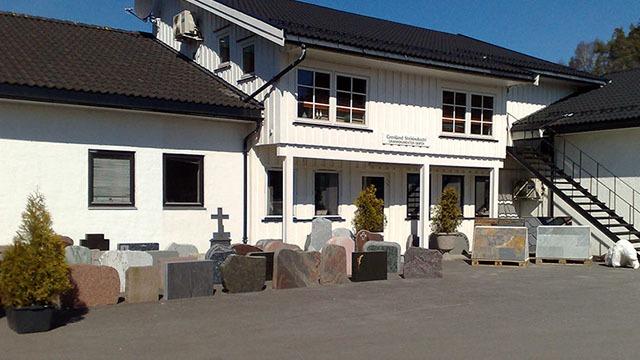 En bygning med hvit fasade og flere gravsteiner plassert foran, under en klar blå himmel.