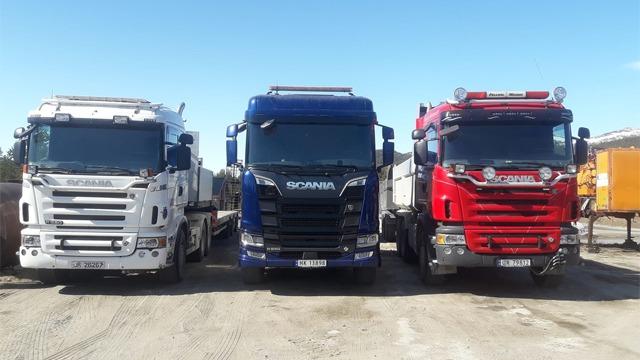 Tre lastebiler parkert på en byggeplass, med en hvit, en blå og en rød Scania-lastebil.