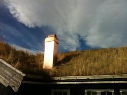 Kobberpipe på taket av en hytte med gressdekket tak under en blå himmel med skyer.