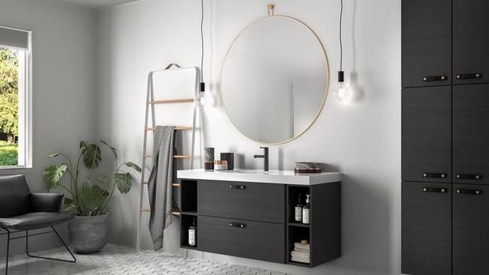 Moderne bad med svart skap, speil med gullramme og planter i et lyst rom.